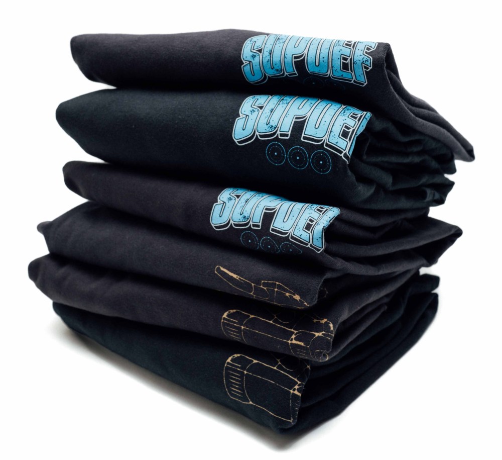 A neatly stacked pile of black t-shirts featuring the word 'SUPDEFI' in blue and illustrations on the front.